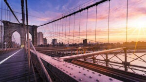 view from on the Brooklyn Bridge looking over the East River at sunset with city skyline in background in NYC, New York, USA